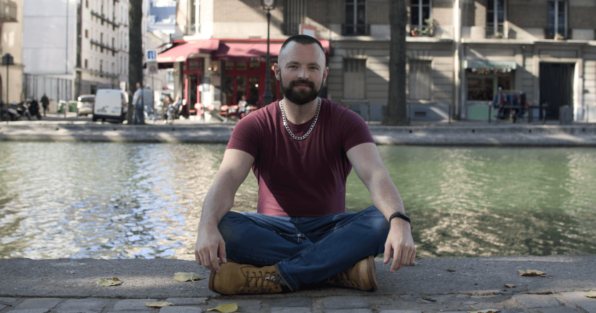 Dan Edwards sitting cross-legged by a canal in a burgundy shirt