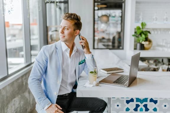 Professional man in light blue blazer talking on phone at desk with laptop